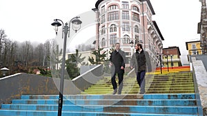 Successful businessmen walking down the stairs in rainy weather near beautiful historic building and autumn forest. Stock