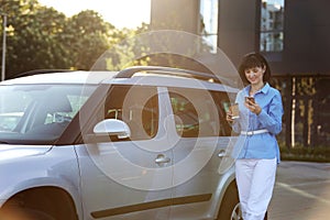 Successful businesswoman in blue shirt, white pants with paper cup of coffee, texting on smartphone while walking to the