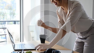 Successful businesswoman looking at laptop computer and raising her arm up to celebrating her achievement.