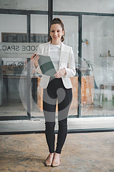 Successful businesswoman standing in creative office and looking on camera.