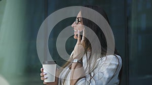 Successful businesswoman is talking on phone, holding coffee cup outdoors.