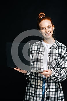 Successful cheerful young woman holding laptop computer and looking at camera on black background.