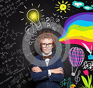 Successful clever child boy with ginger hair, glasses and crossed arms on lightbulb, science and arts scetch background.