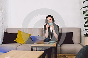 Successful confident middle aged female teacher having cup of coffee before online lesson, sitting in front of laptop, using