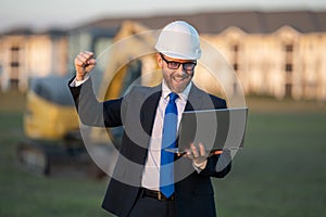 Successful construction business owner. Construction worker in suit and helmet near excavator. Confident construction