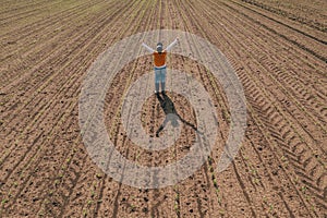 Successful corn farmer wearing trucker`s hat standing in corn sprout field with arms raised up in the air as gesture of victory,