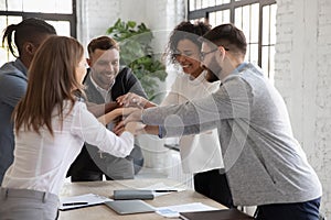 Successful diverse employees stacking hands, engaged in team building