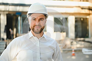 Successful engineer or architect, crane and building construction at backgrpound. Joyous businessman wearing helmet