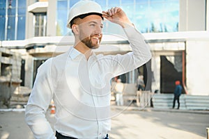 Successful engineer or architect, crane and building construction at backgrpound. Joyous businessman wearing helmet