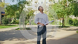 Successful engineer holding project examining houses at summer neighbourhood