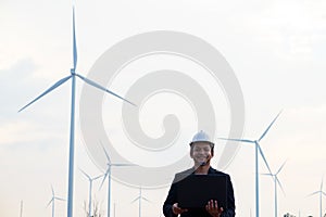 Successful engineer man standing and using computer labtop with wind turbine