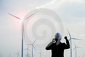 Successful engineer standing and hoding smartphone with wind turbine photo