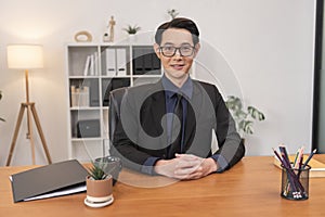 Successful executive Asian businessman sitting on desk in office. Smiling middle aged man working in a corporate