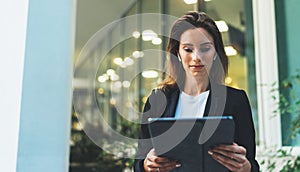 Successful female banker using tablet and wireless earphones outdoors near his office background lights, portrait young woman