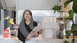 Female business owner standing behind counter of coffee shop and smiling to camera.