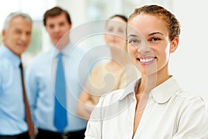 Successful female executive with her team in background. Successful young female executive smiling with her staff in