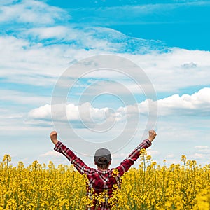 Successful female farmer wearing plaid shirt and trucker`s hat with arms raised in the air in victorious pose standing in bloomin