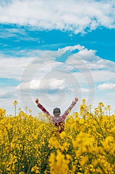 Successful female farmer wearing plaid shirt and trucker`s hat with arms raised in the air in victorious pose standing in bloomin