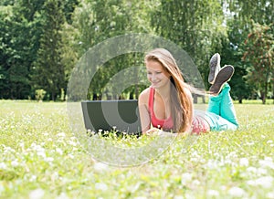 Successful girl online. Beautiful young woman with notebook in the park. Happy student lying on grass with laptop. Outdoor.