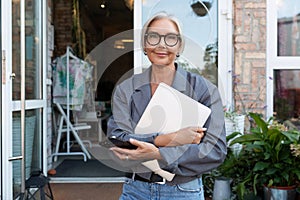 successful gray-haired senior business woman with a stylish hairstyle and glasses holds a laptop and walks around the