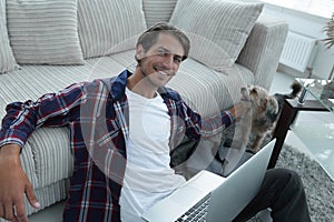 Successful guy stroking his pet sitting on the floor near the sofa