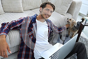 Successful guy stroking his pet sitting on the floor near the sofa