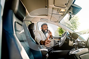 Successful handsome African man businessman and boss sitting in the car, talking on the phone, smiling, looking at