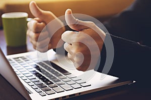 Successful handsome businessman sitting in front of laptop, showing thumbs up in modern office.