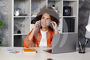 Successful happy African American business woman talking on a mobile phone sitting at workplace in modern office or coworking