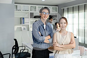Successful happy asian businessman and businesswoman smiling arms crossed standing at modern office looking at camera. business