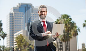 successful happy businessman in suit working on laptop standing outdoor, office worker