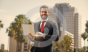 successful happy businessman in suit working on laptop standing outdoor, office worker