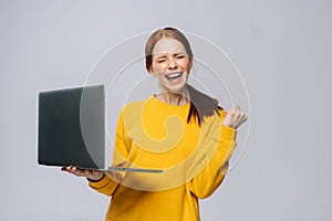 Successful happy shocked young woman with closed eyes holding laptop computer