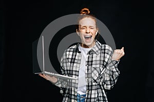 Successful happy shocked young woman with open mouth and closed eyes holding laptop computer