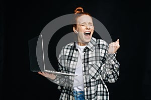 Successful happy shocked young woman with open mouth and closed eyes holding laptop computer