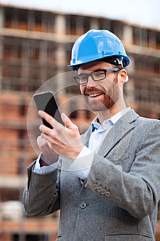 Successful young architect or businessman standing at the construction site, browsing internet