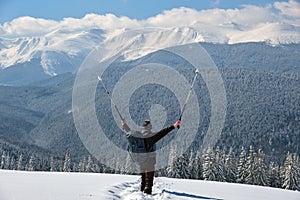 Successful hiker with backpack walking on snowy mountain hillside on cold winter day