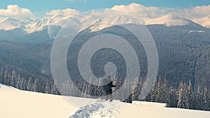 Successful hiker with backpack walking on snowy mountain hillside on cold winter day.