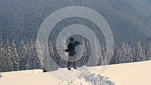 Successful hiker with backpack walking on snowy mountain hillside on cold winter day