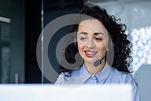 Successful hispanic woman with headset phone for video call working with laptop while sitting at workplace, online