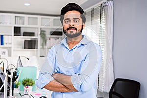 Successful Indian businessman entrepreneur in casual smiling and looking at the camera while standing with his arms crossed.