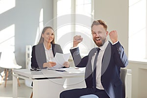 Successful interview. A man in a suit rejoices at a new job sitting at a table with a woman employer in a white office.