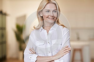 Successful lady. Portrait of elegant mature woman wearing white shirt smiling aside while posing with arms crossed for