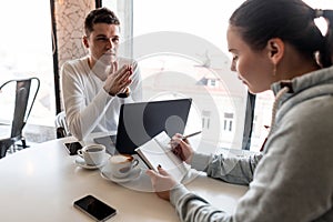 Successful leader and business owner leads an informal business meeting in a cafe.Young woman takes notes on a notepad