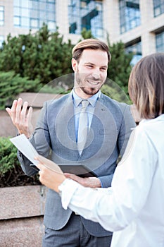 Successful male and female business people talking in front of an office building, having a meeting and discussing