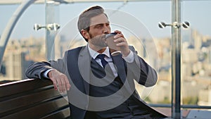 Successful man enjoying coffee on glass terrace. Calm boss in suit rest morning