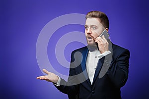 Successful man in tuxedo and bow tie talking on phone. businessman holding smartphone, blue background