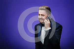 Successful man in tuxedo and bow tie talking on phone. businessman holding smartphone, blue background