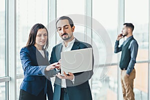 Successful man and woman making business plan, comparing annual data in laptop, while their coleague is on phone on