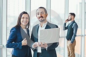 Successful man and woman making business plan, comparing annual data in laptop, while their coleague is on phone on